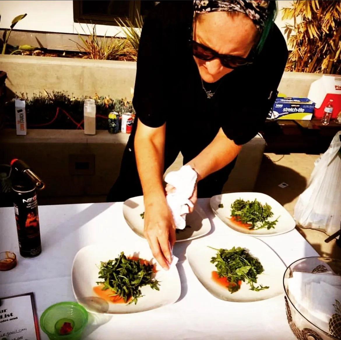 Chef Chelsea Goins carefully plating a dish in a professional kitchen